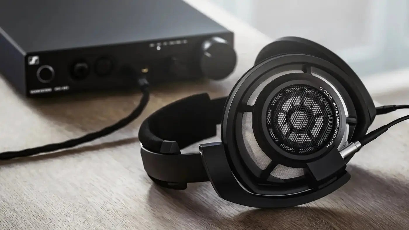 Open back headphones resting in front of a headphone amplifier on a timber table