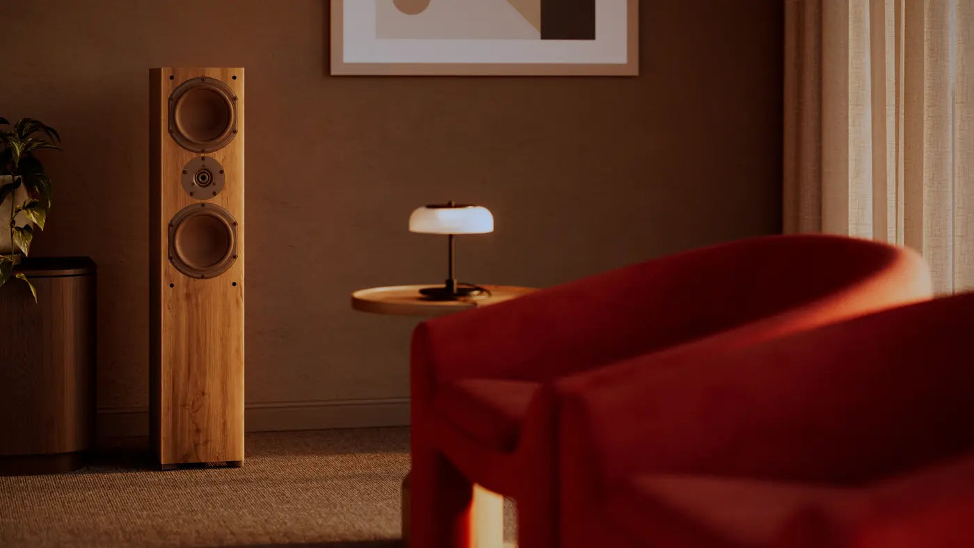 A walnut Krix tower speaker beside a red velvet armchair in a warm lounge